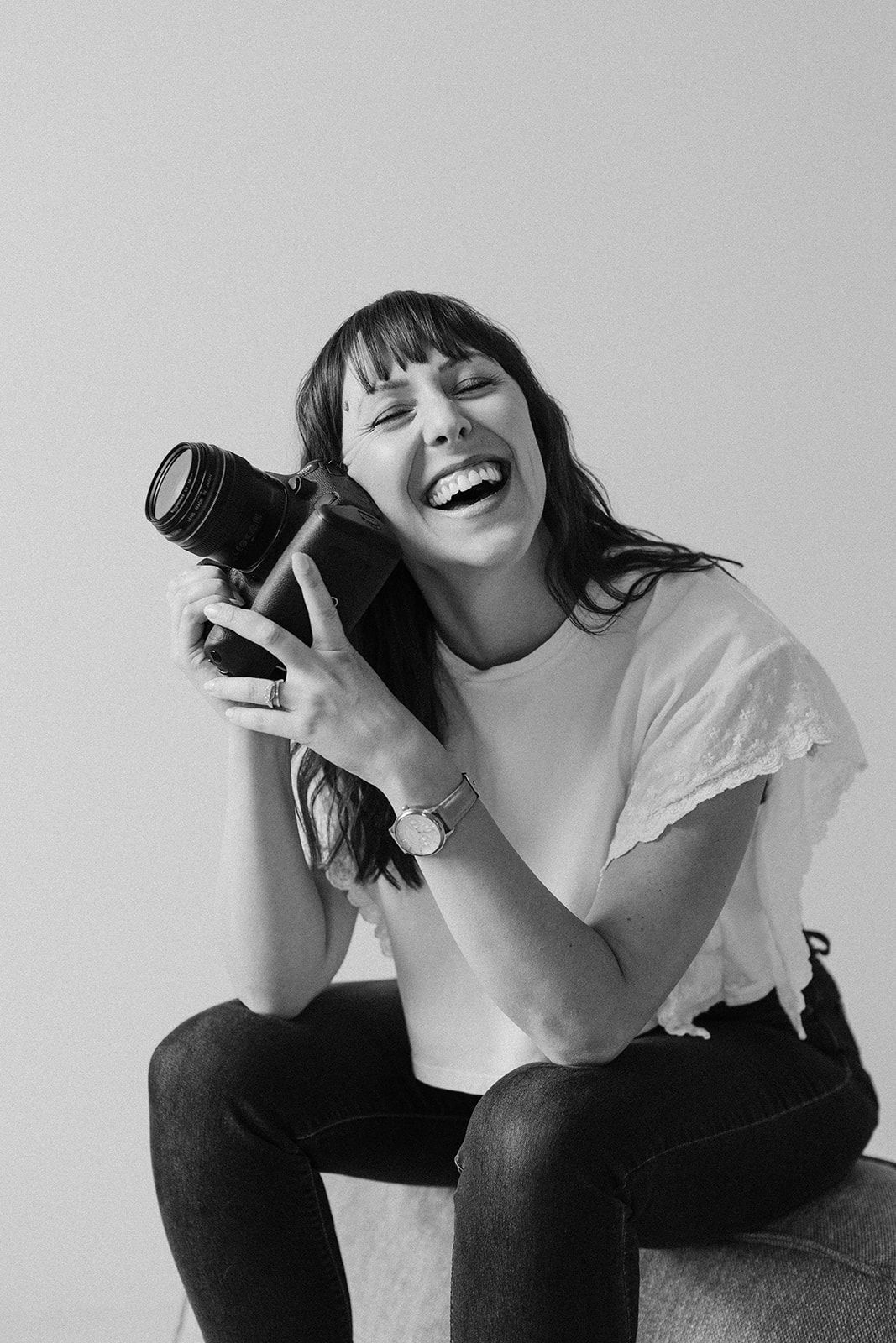 A photographer holding a vintage camera laughs joyfully during a lifestyle photoshoot.
