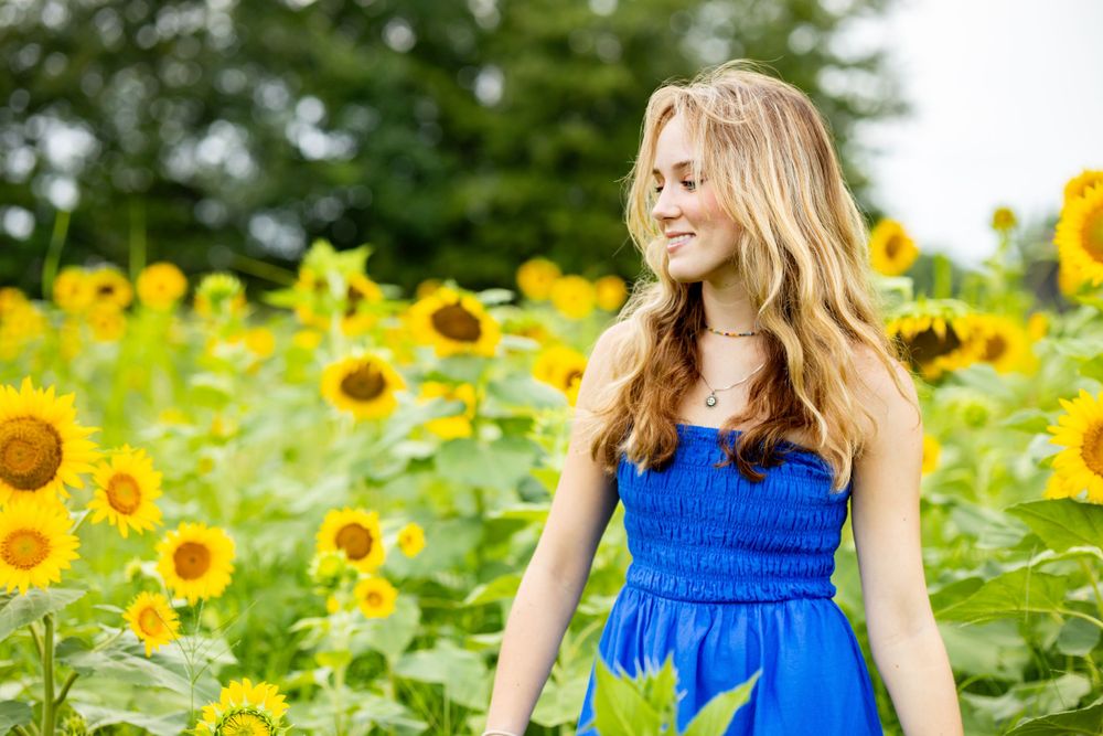 Woman in bright blue sundress poses among blooming sunflower field during summer.