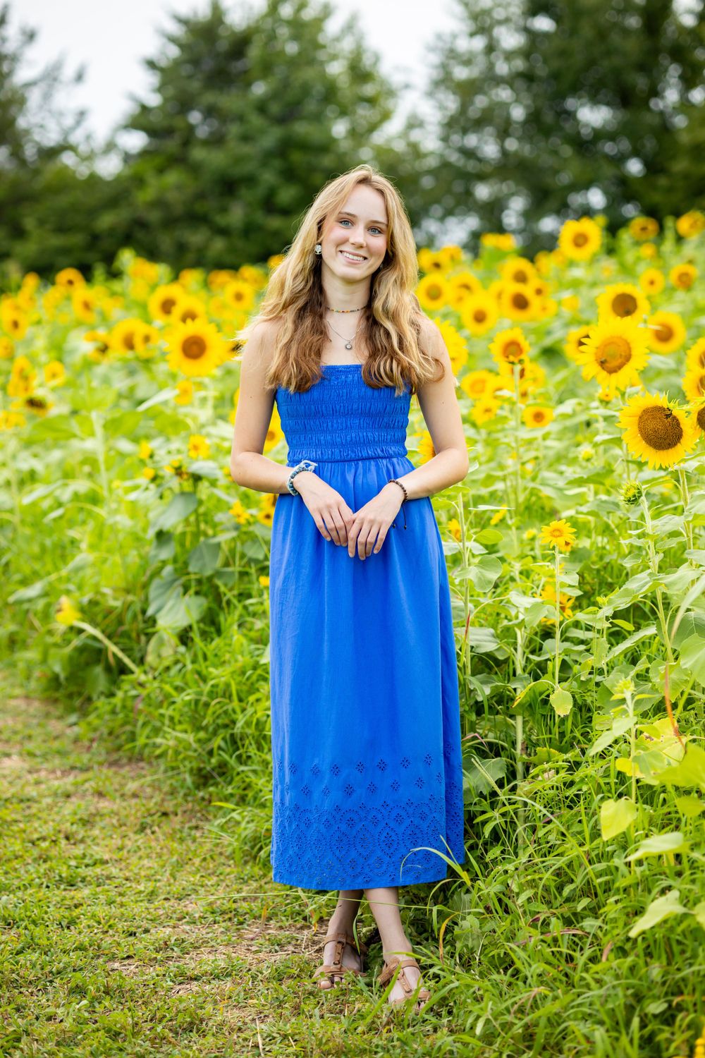 Portrait in sunflower field wearing blue maxi dress on dirt path.