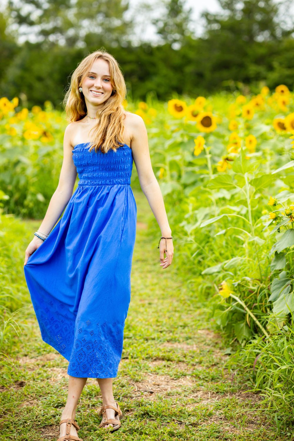 Summer fashion portrait on path through blooming sunflower field.