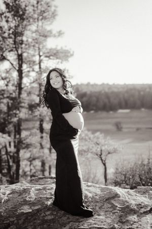 A black flowing maternity gown creates dramatic contrast against a scenic mountain overlook.