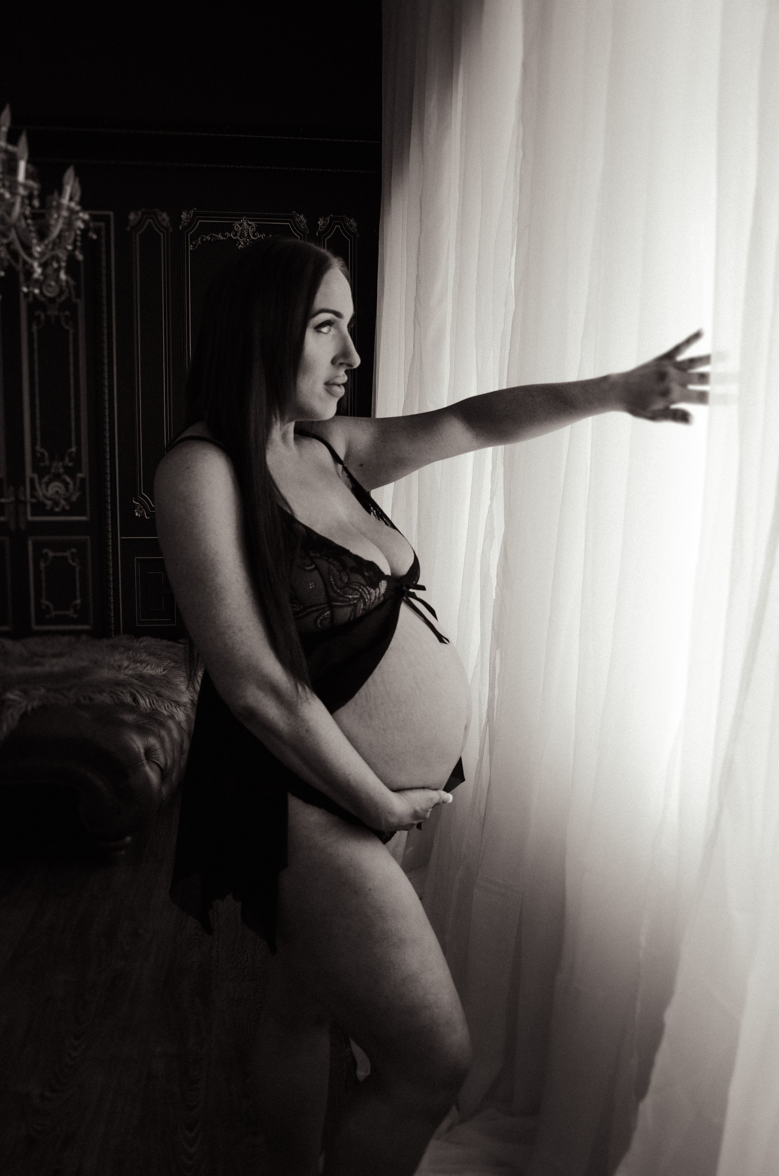 A black and white boudoir maternity photo near a window with natural light.