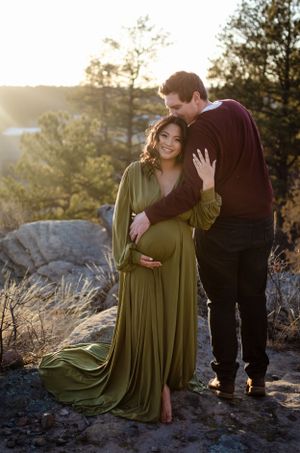 A couple shares an intimate moment on a rocky overlook during their maternity photoshoot.