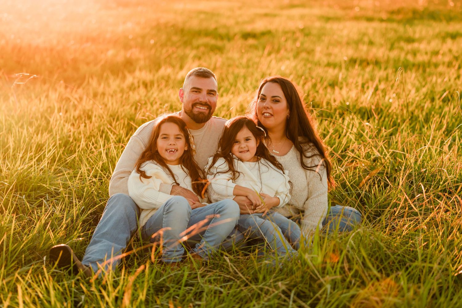 Family portrait in tall grass field during golden hour sunset.