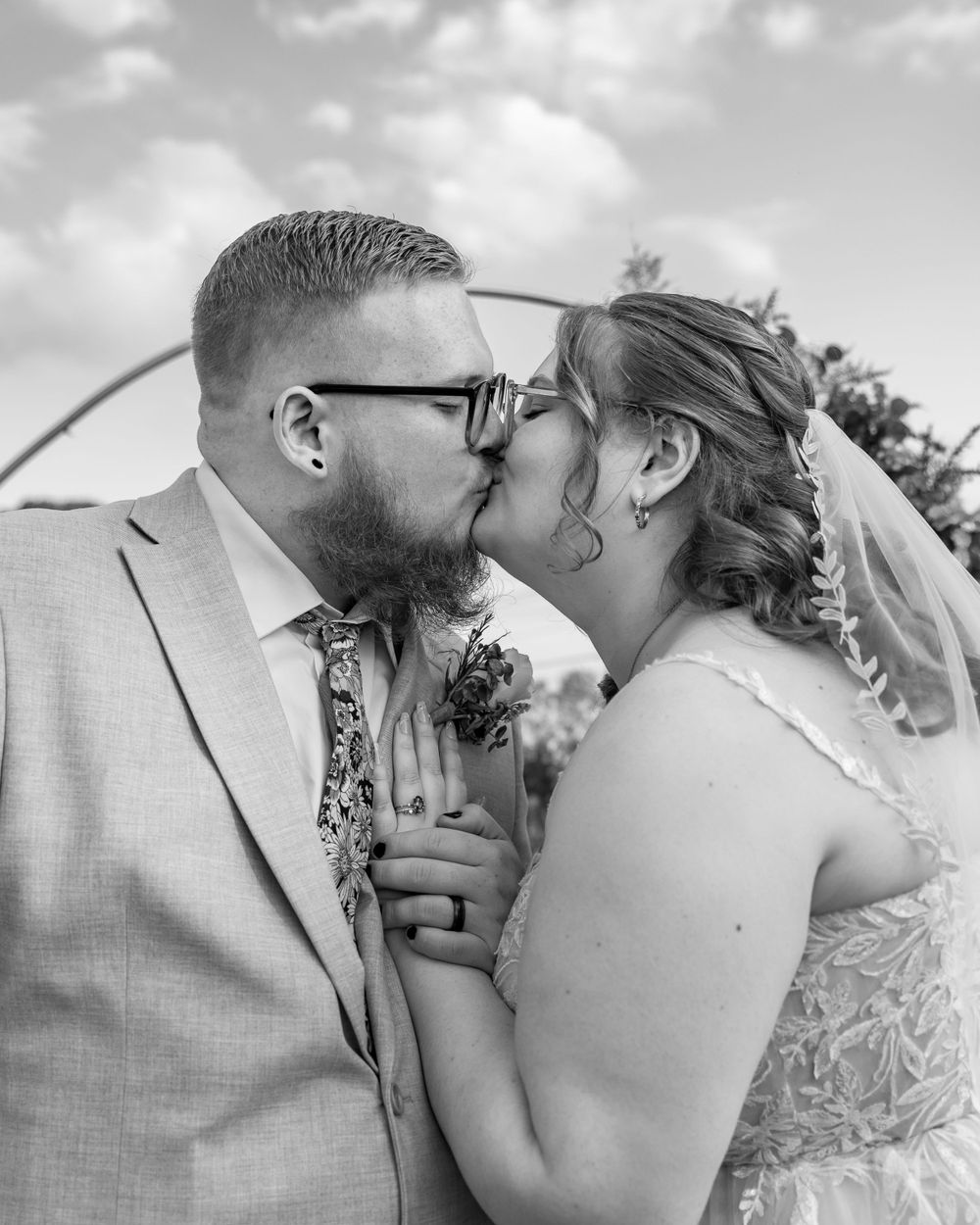 A romantic black and white wedding photo captures a tender kiss between a bride and groom outdoors.