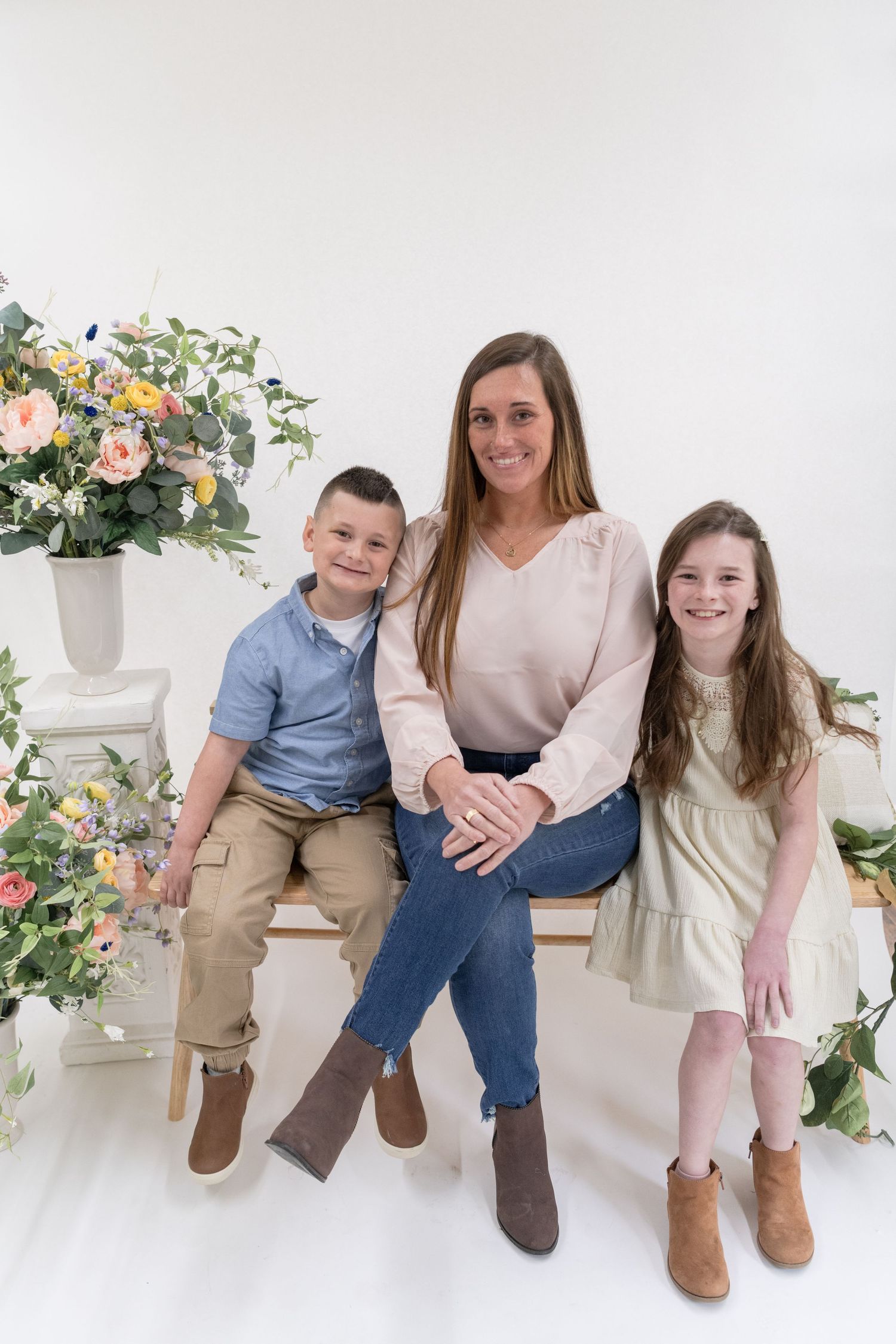 Family portrait with children in coordinated neutral outfits against white floral backdrop.