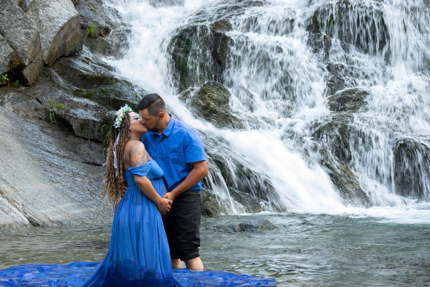 Couple in blue attire embracing in front of cascading waterfall.