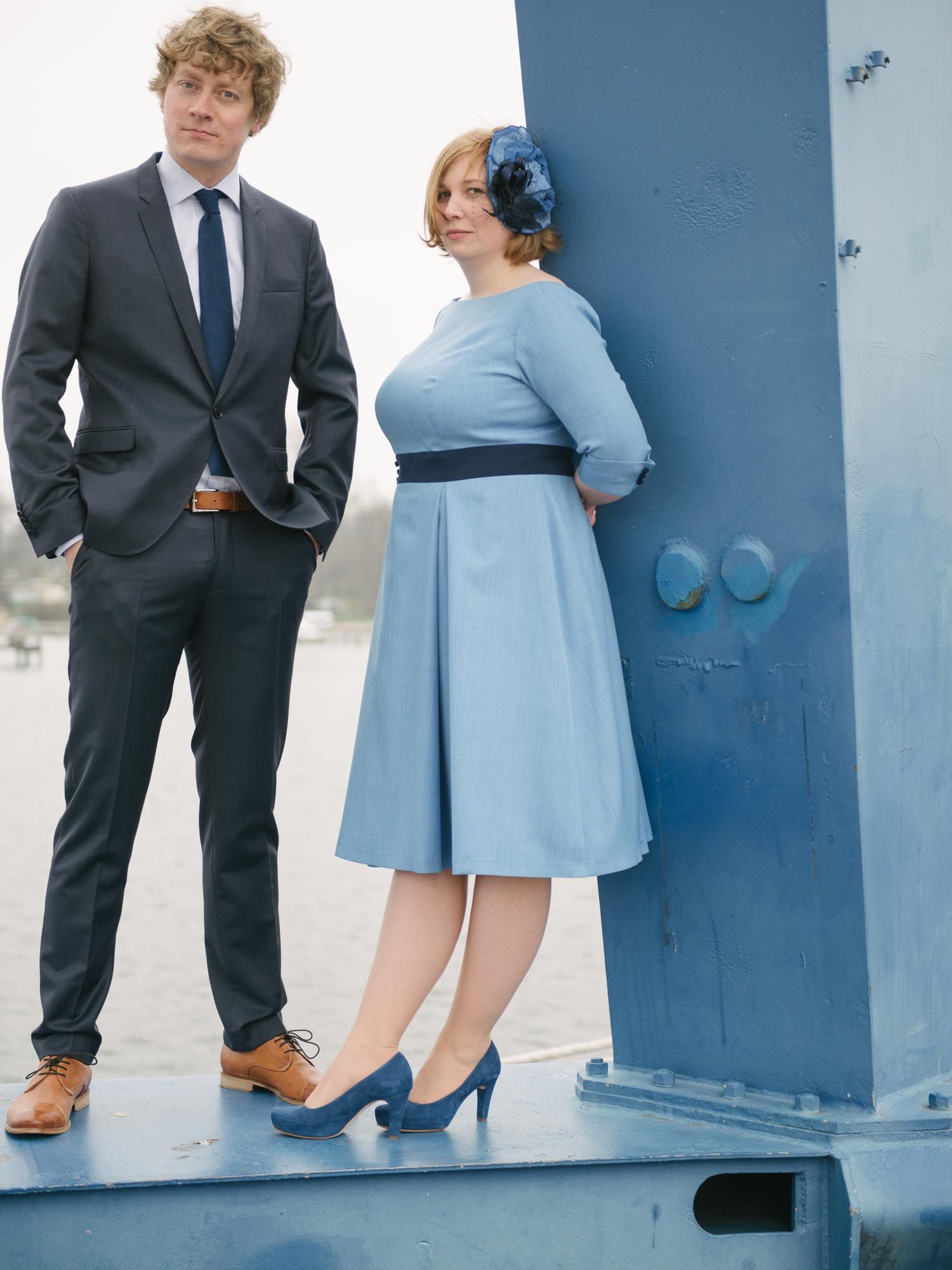 A couple in vintage-inspired formal wear posing against a blue wall.