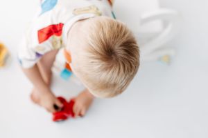 Overhead view of young child playing with colorful toys on white surface.