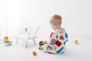 Toddler in patterned pajamas playing with toys on white floor.