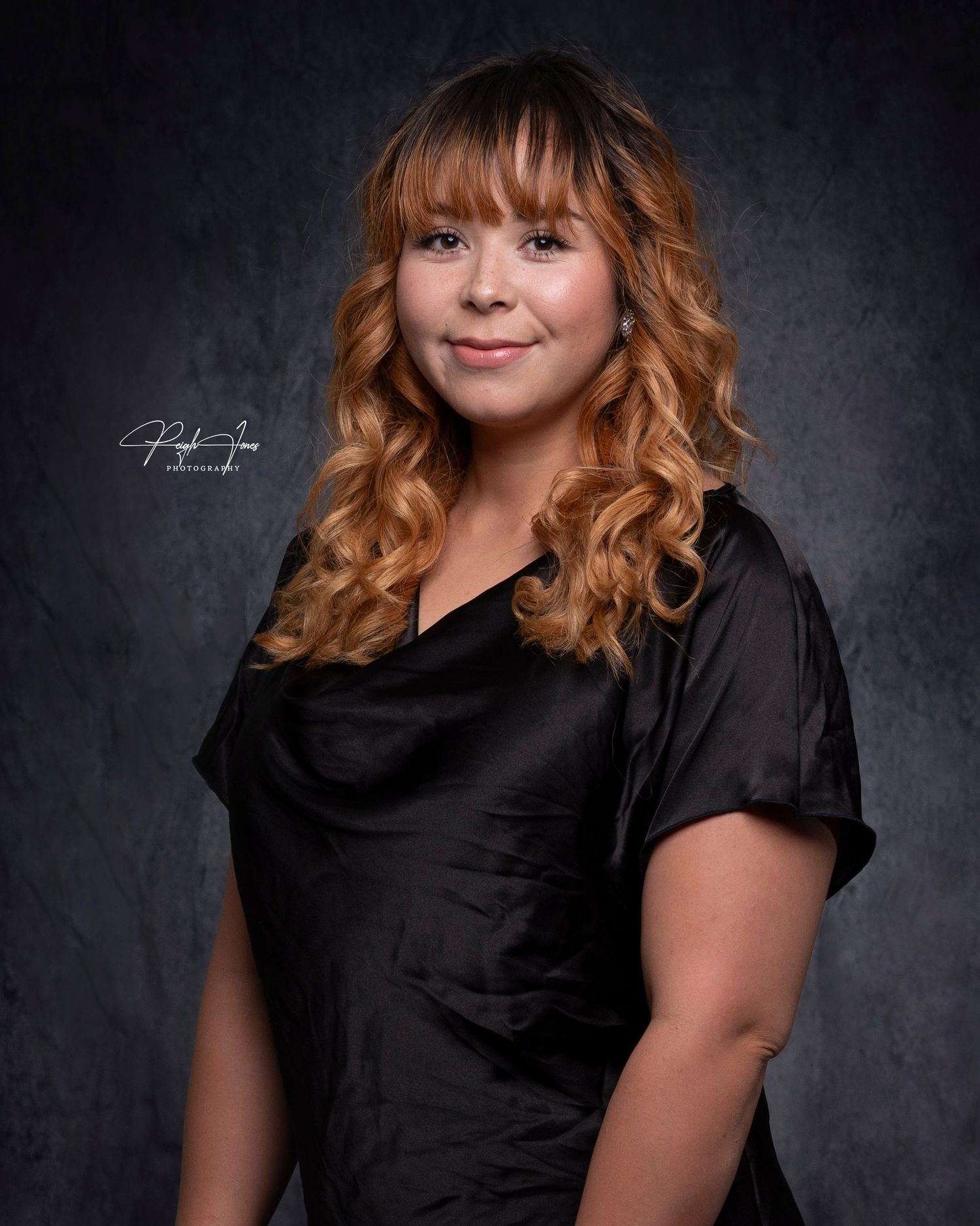 Woman with ombre curly hair smiles in black top for professional studio portrait.