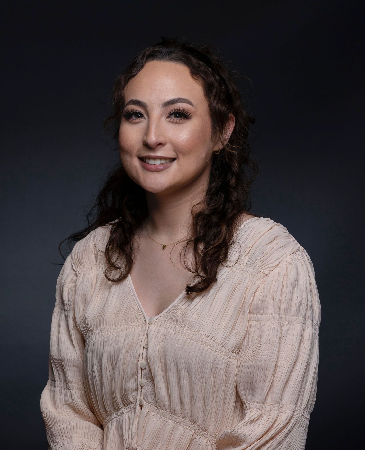 Young woman with curly dark hair smiles in cream blouse for professional headshot portrait.