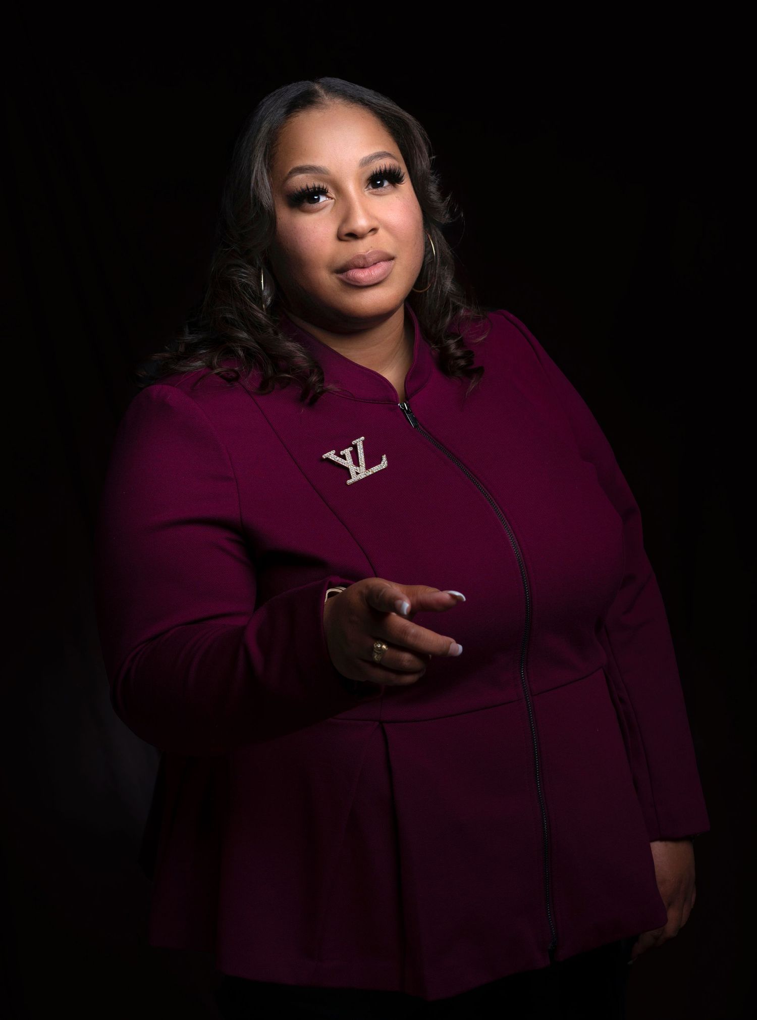 Confident woman in magenta Louis Vuitton jacket poses with outstretched hand against black background.