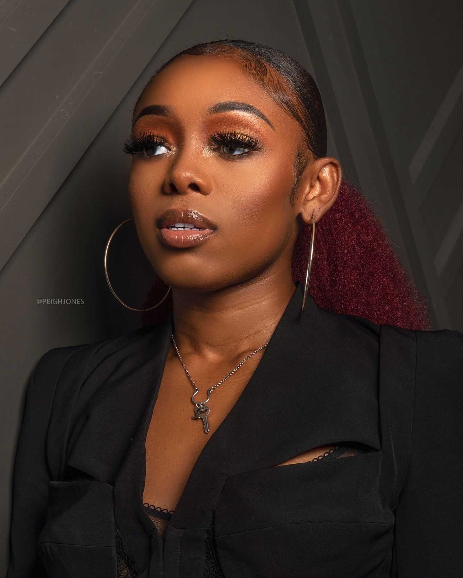 Woman with burgundy highlights and hoop earrings poses in black outfit for stylish portrait.