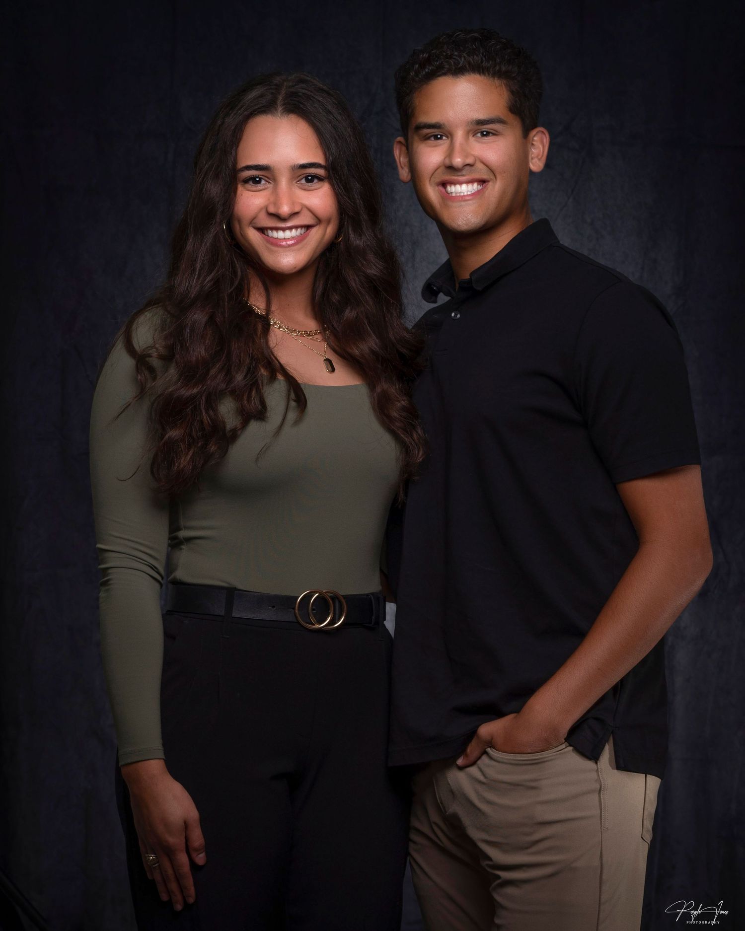 Smiling young couple poses together in casual attire for studio portrait photo.