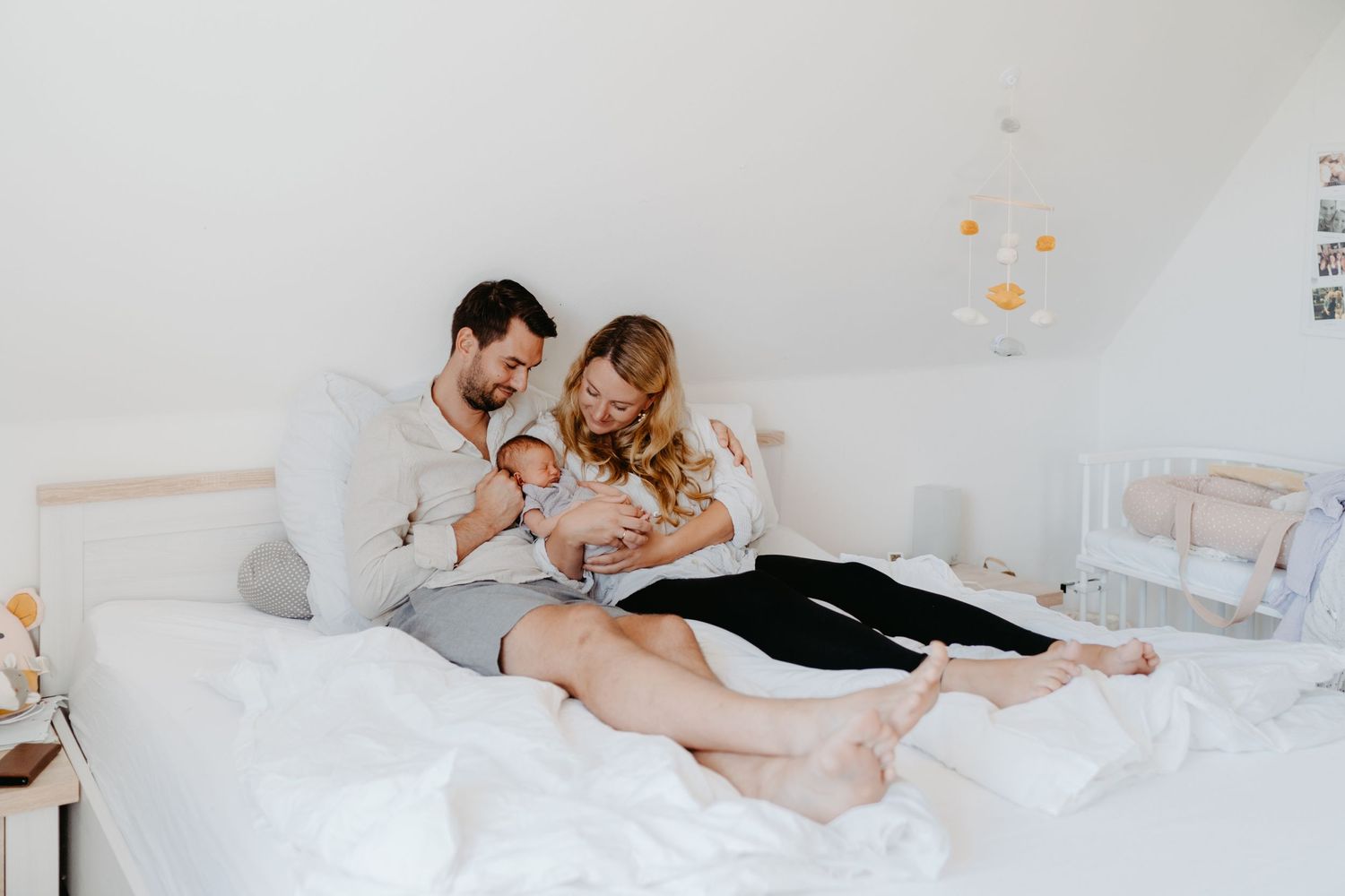Happy family couple in casual clothes cuddling on white bed with their small dog in bright bedroom while a Homestory fotoshooting in Hamburg