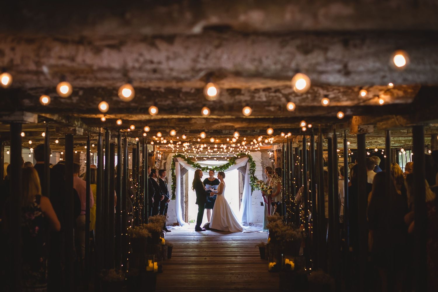 A romantic wedding ceremony venue with string lights illuminating a long hallway with dark pillars.
