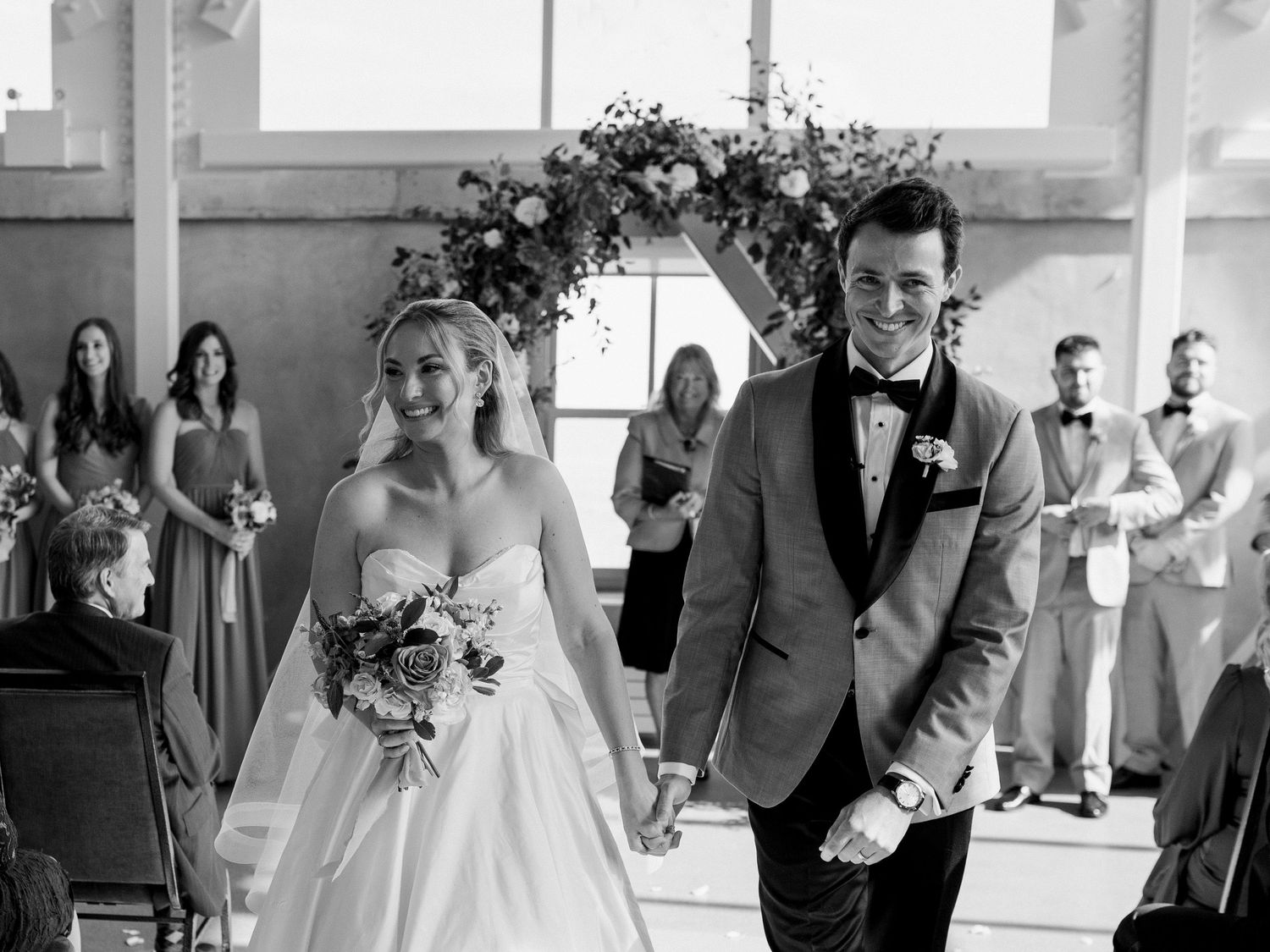 A bride and groom walk down the aisle hand-in-hand and smiling brightly. Photo captured by Katie Crane.