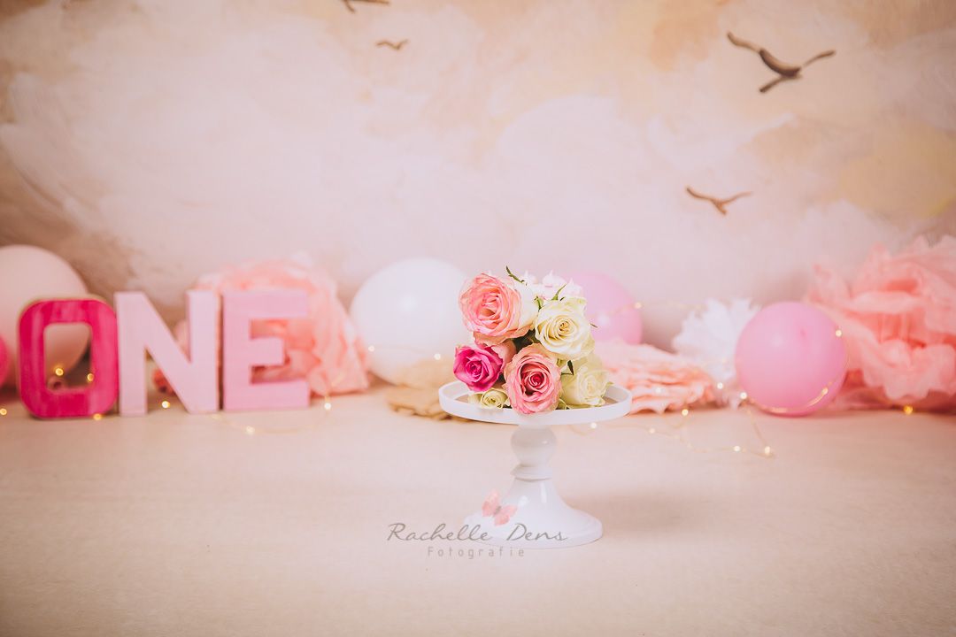First birthday setup with pink 'ONE' letters, roses on cake stand, and flying birds backdrop.
