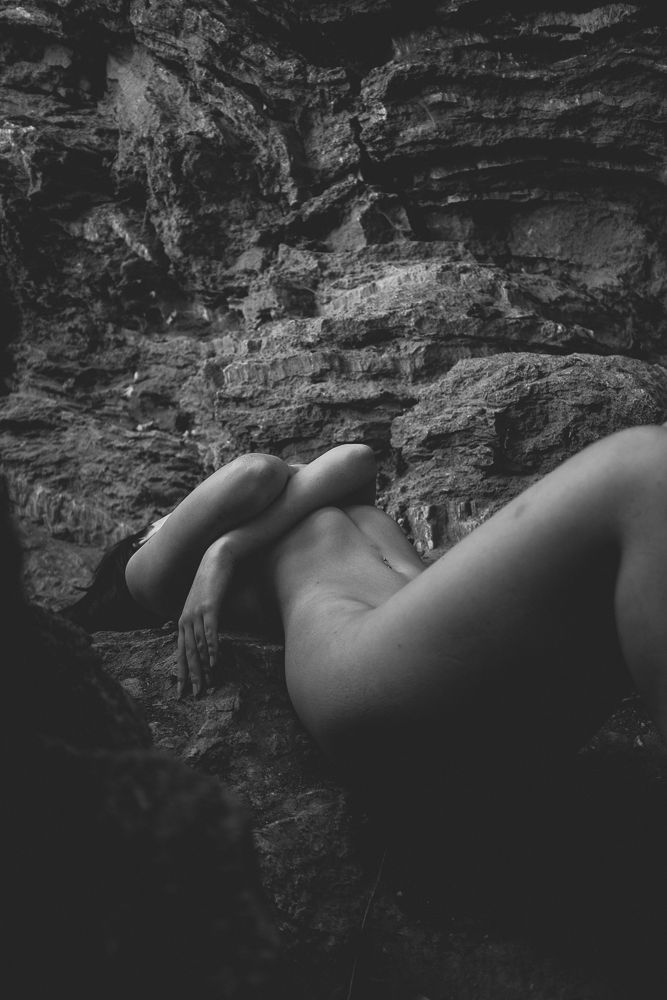Artistic black and white nude figure against textured rock wall surface.