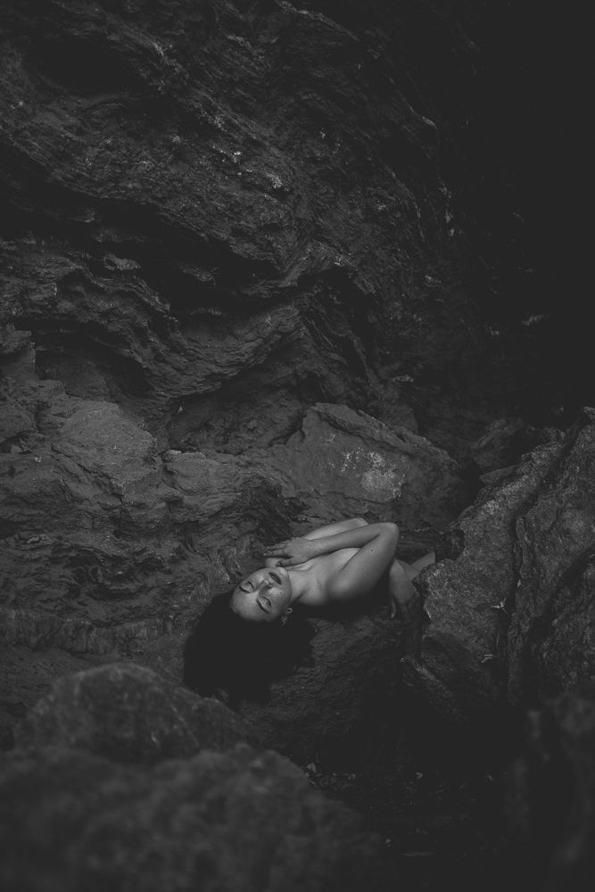 Dramatic monochrome photograph of figure resting in rocky cave environment.