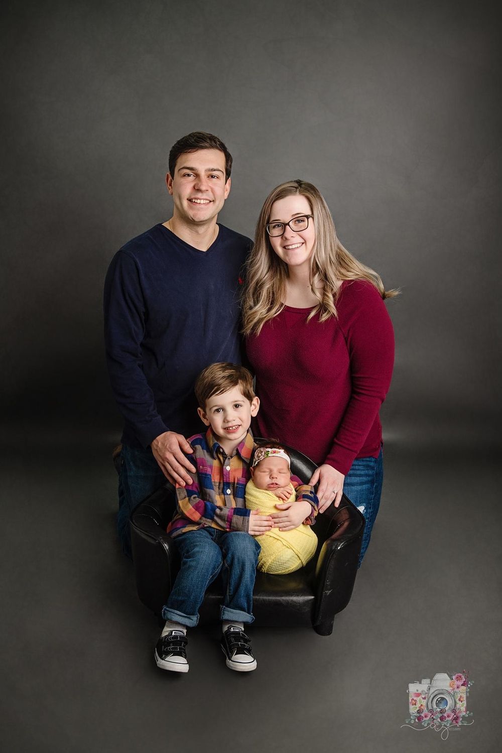 Professional studio portrait of a family of four sitting together against a dark background.