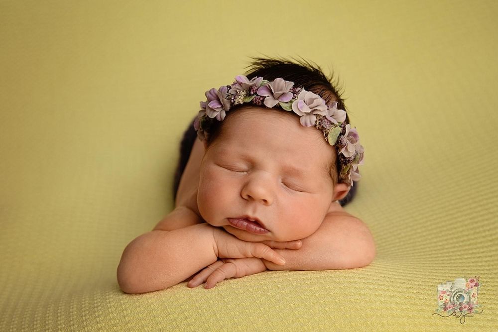Peaceful newborn portrait with floral headband resting on yellow background.