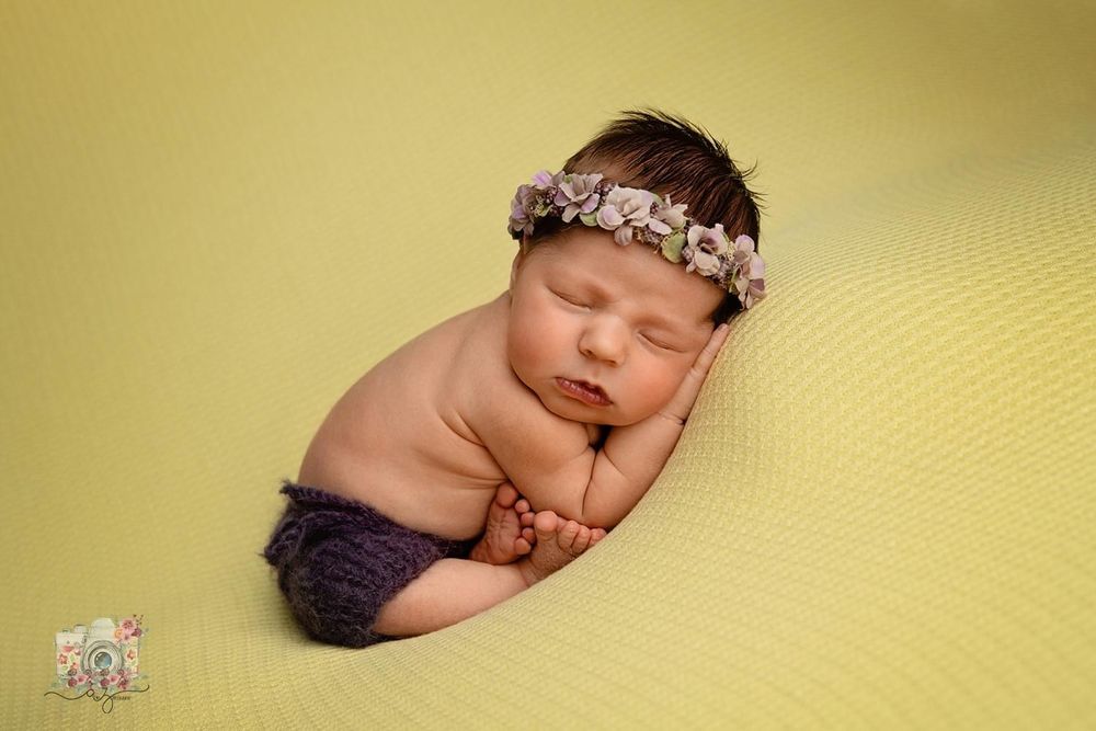 Sleeping newborn wearing floral headband on yellow backdrop.