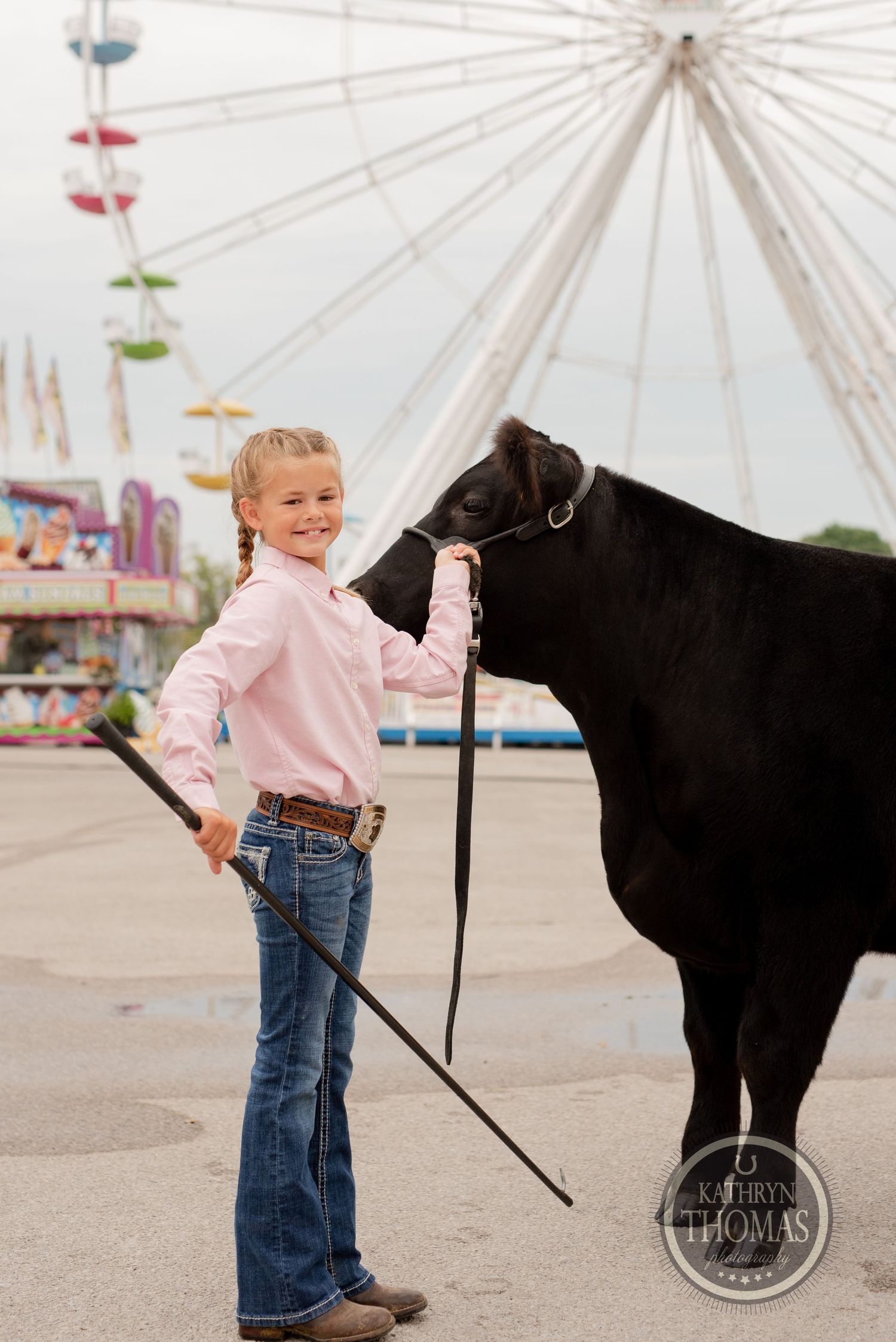 Young exhibitor showing black steer at county fair with ferris wheel in background.