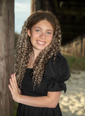 A curly haired girl in a black dress posing under a dock.