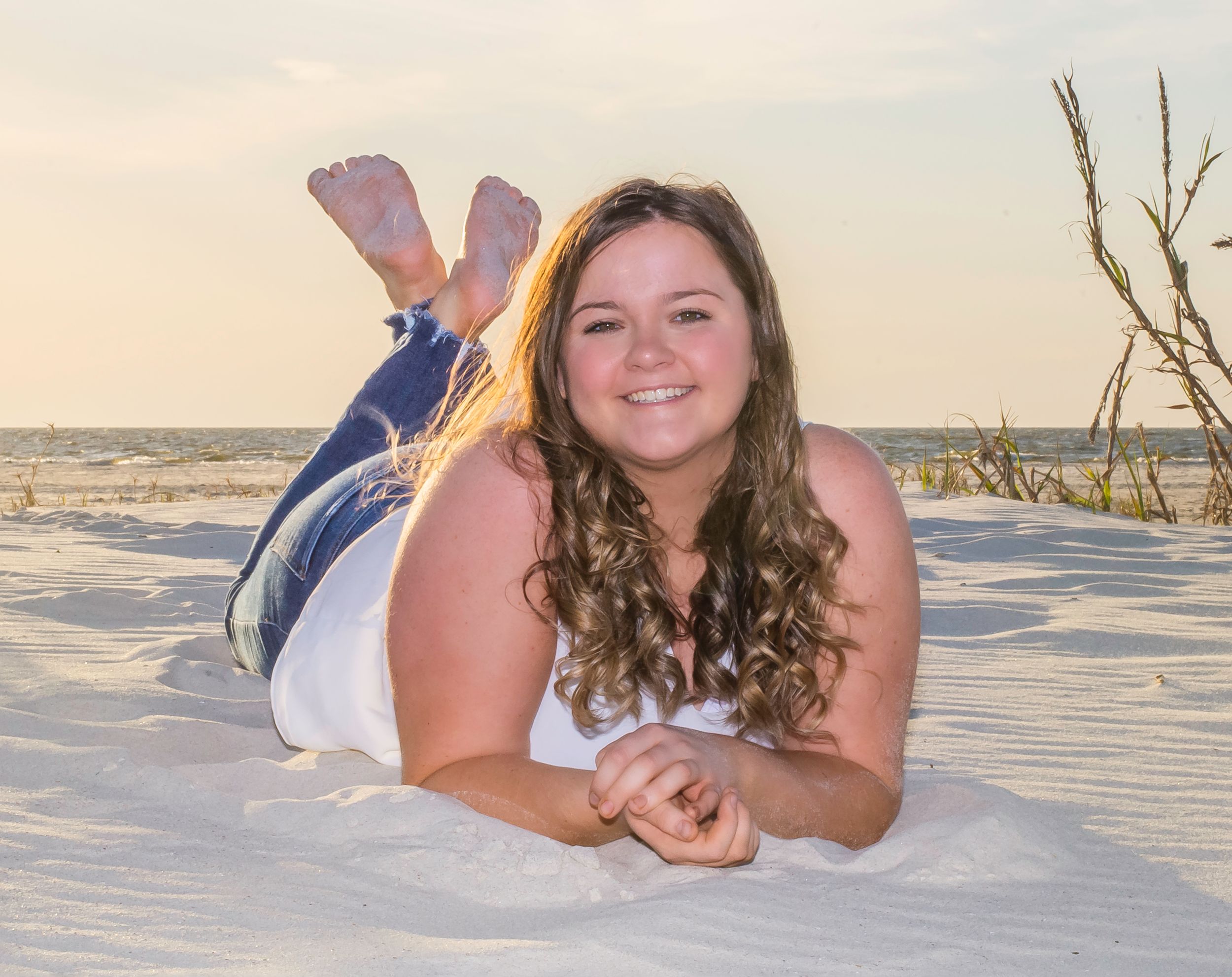 A young woman in a white shirt and jeans posing in the sand.