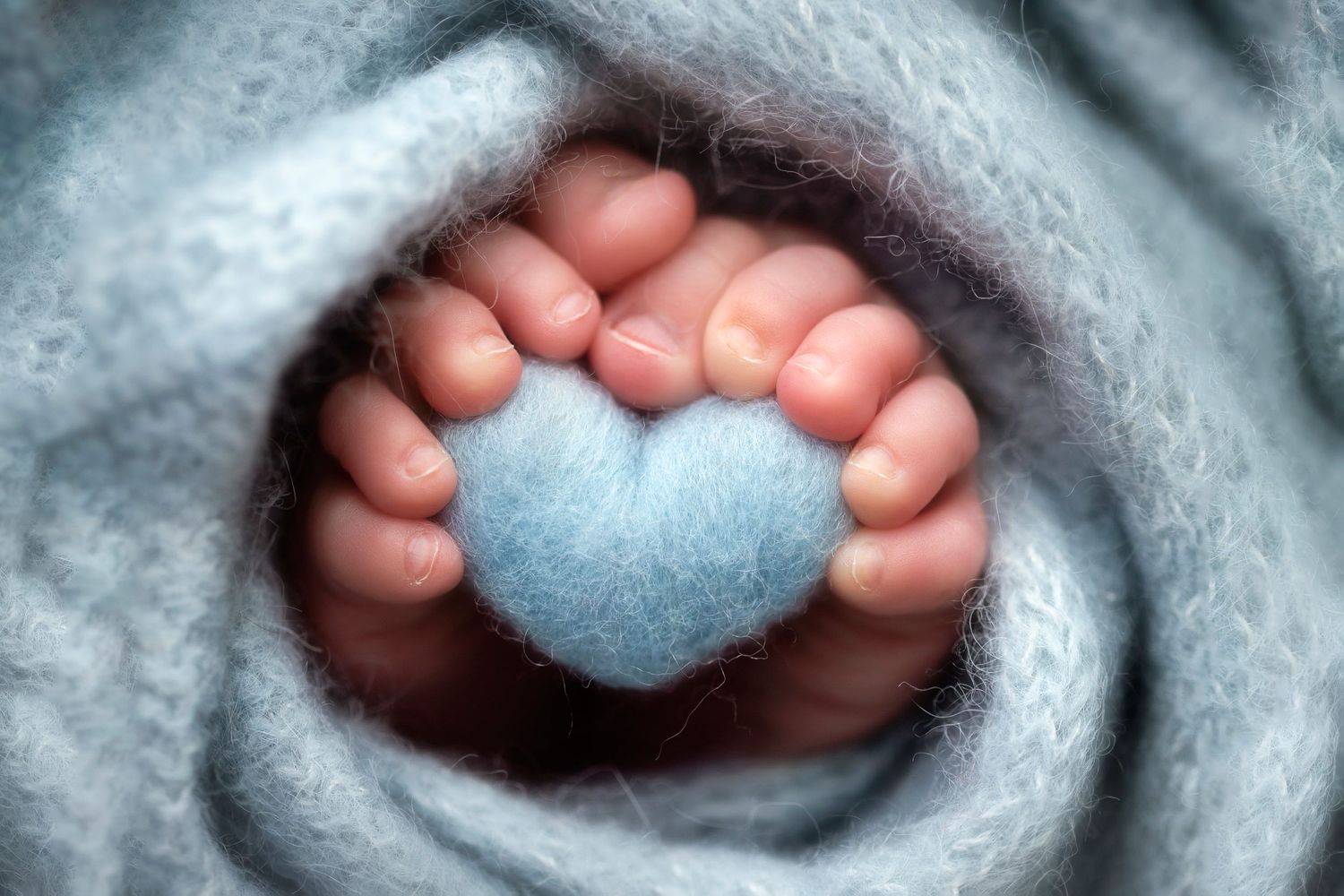 Close-up of tiny baby feet forming heart shape against blue blanket background.
