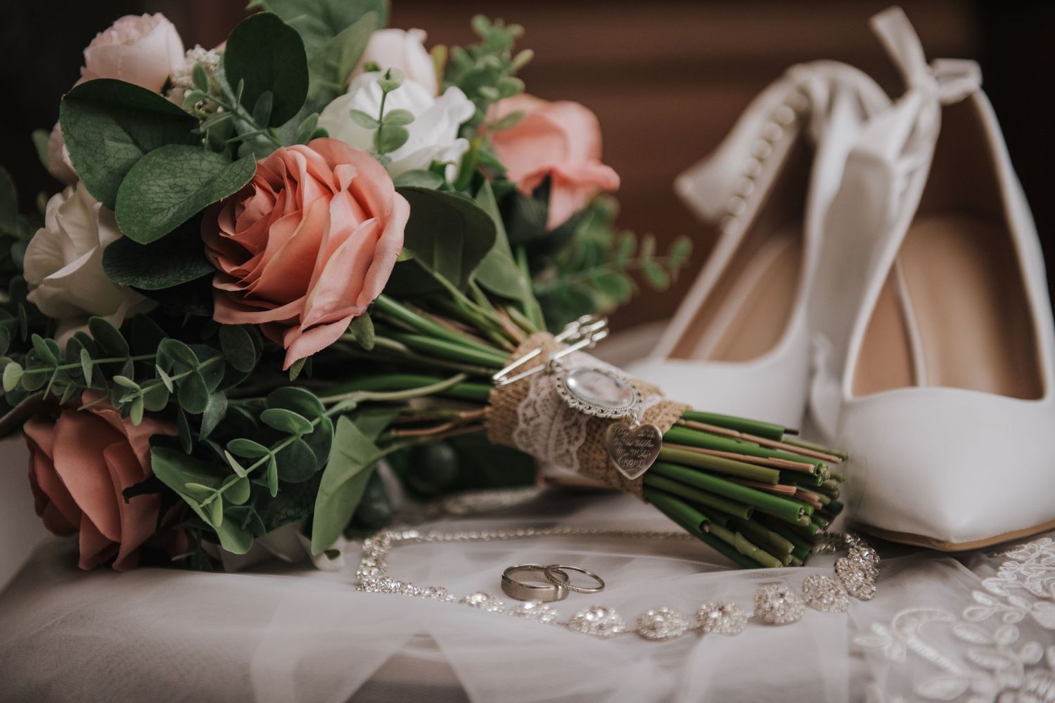 Wedding details featuring pink roses, white heels, and rings on delicate lace.