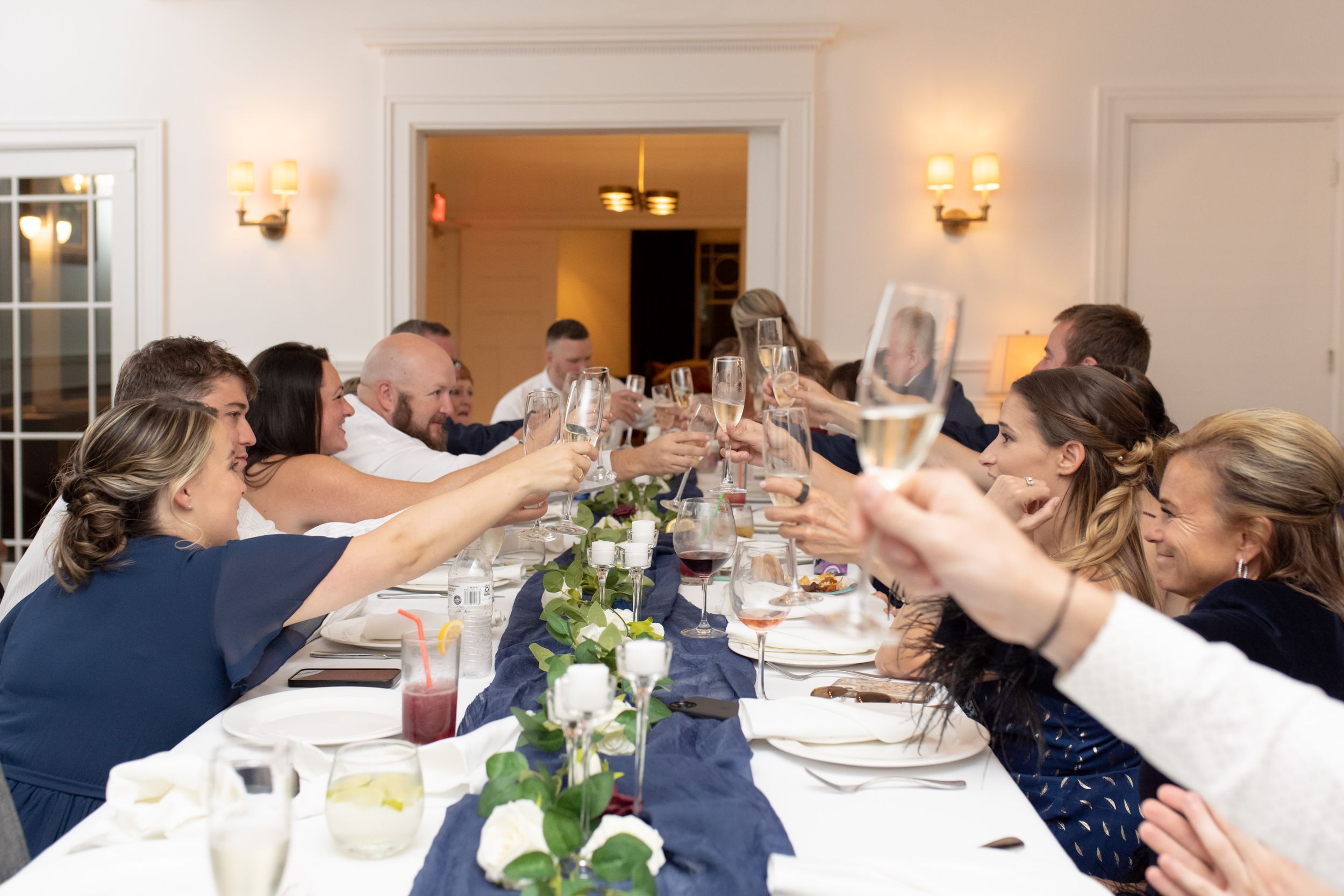 Wedding reception dinner table with navy linens and raised glasses in toast.