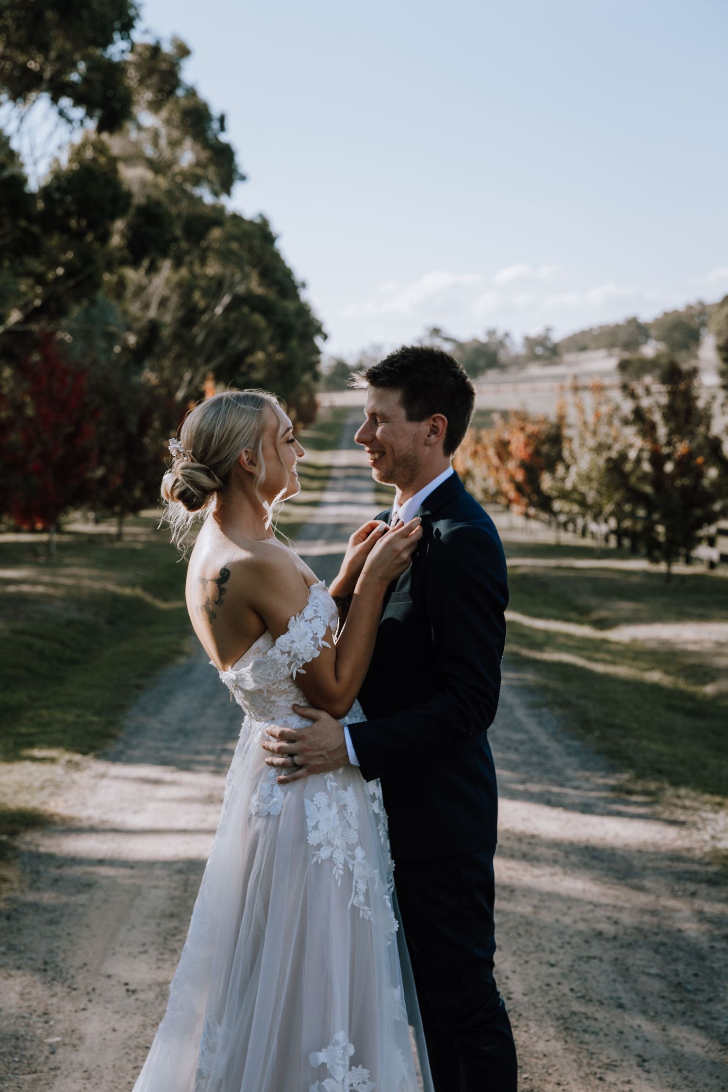 A couple shares a romantic moment on their wedding day on a tree-lined path wearing traditional wedding attire.