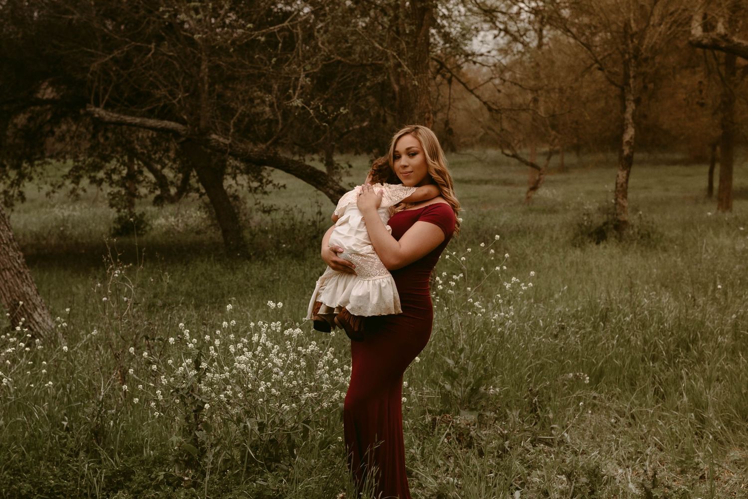 Mother and child share a tender moment in a field of white wildflowers at dusk.