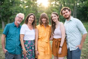 Multi-generational group poses together outdoors at sunset among trees.