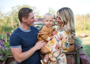 Family shares tender moment outdoors with baby in floral setting at sunset.