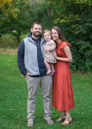 Family portrait on green lawn with fall foliage in background.