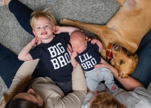 Two siblings in Big Bro and Lil Bro shirts lounging with golden retriever.
