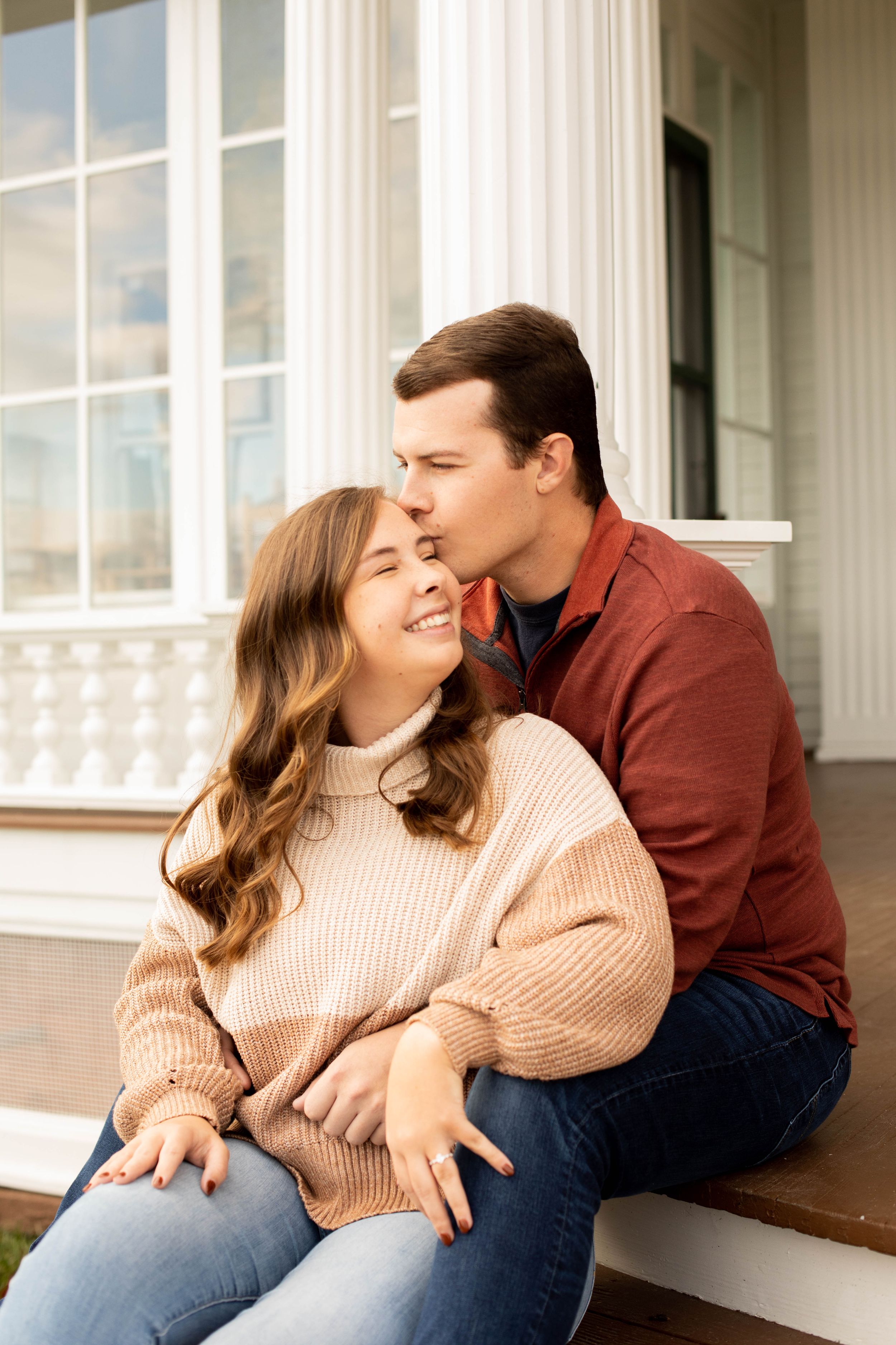 A couple sharing an affectionate moment on white porch steps in casual fall attire.