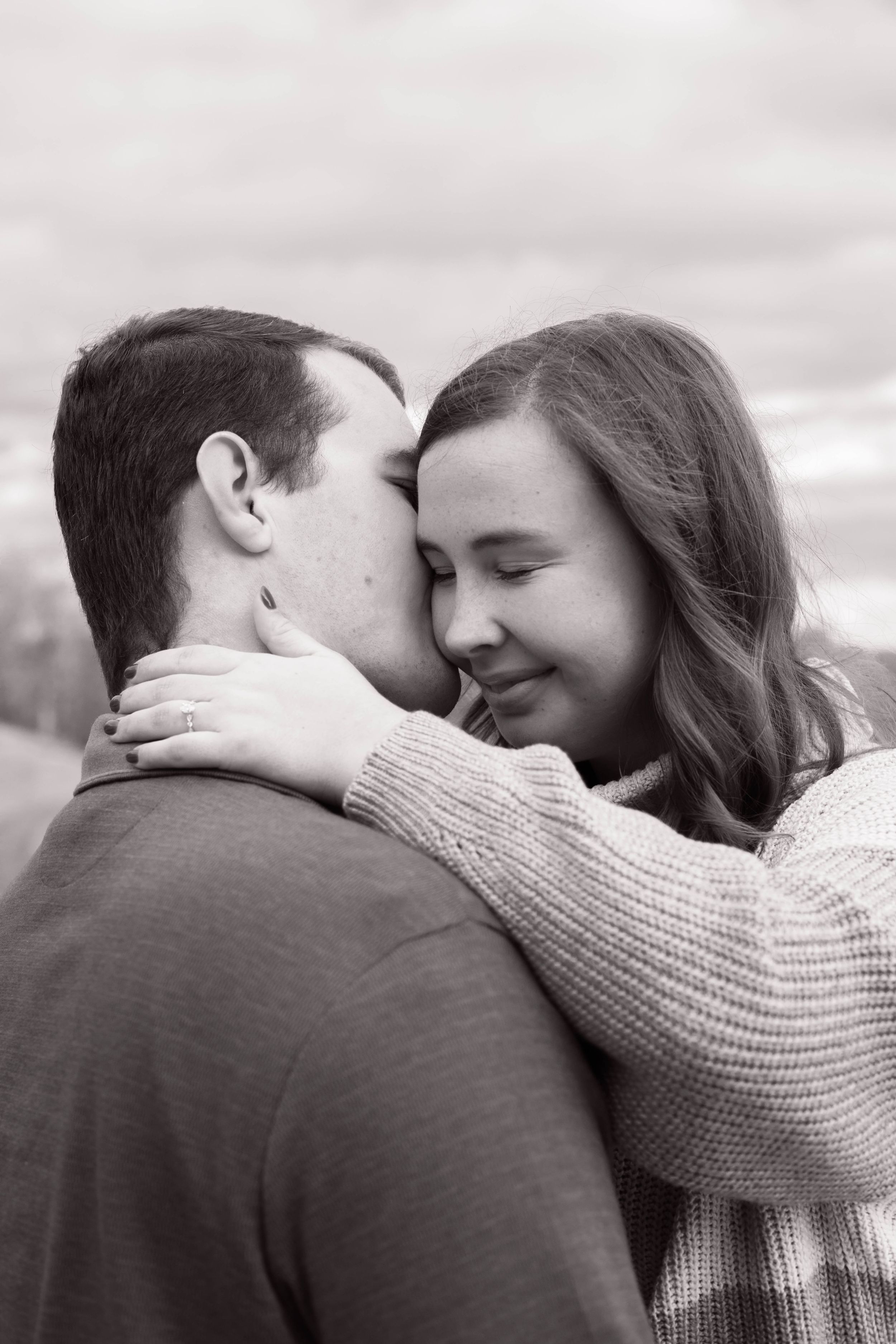 A romantic black and white portrait of a couple embracing with the woman in a knit sweater.