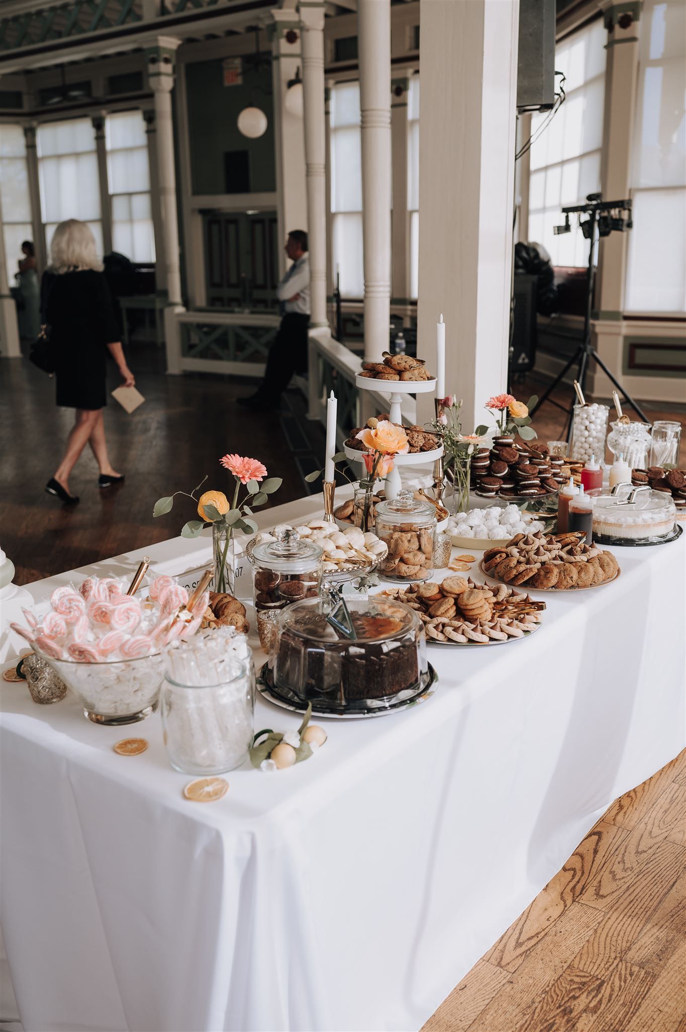 Elegant dessert table with chocolate cake, cookies and various sweets set on white tablecloth at wedding reception.