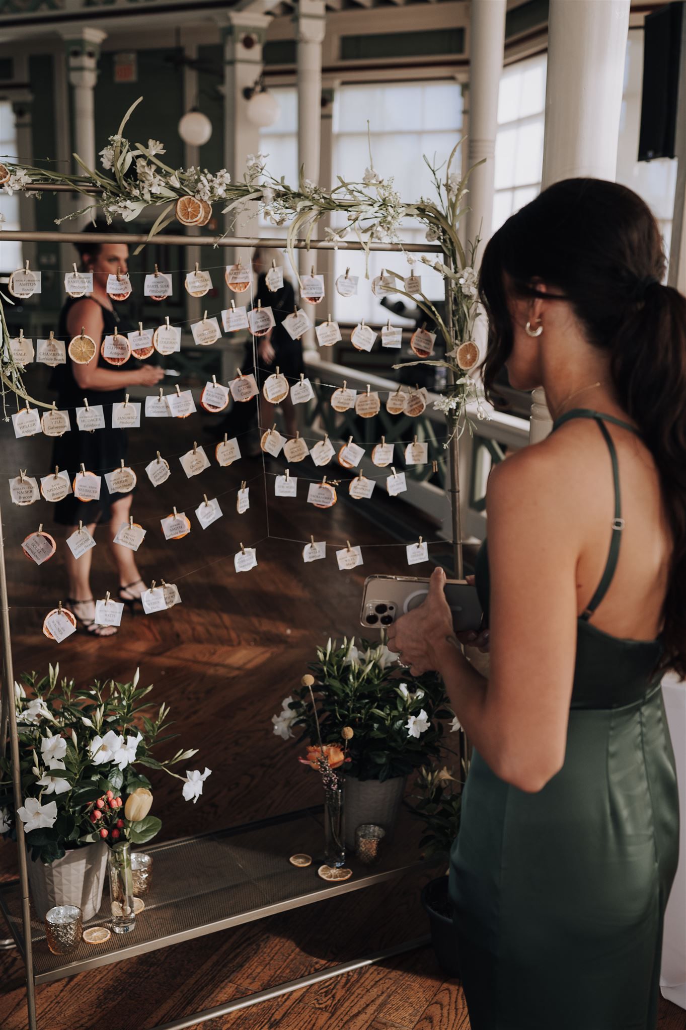 Wedding guest looking at display of escort cards hanging from greenery decorated branches at elegant venue.