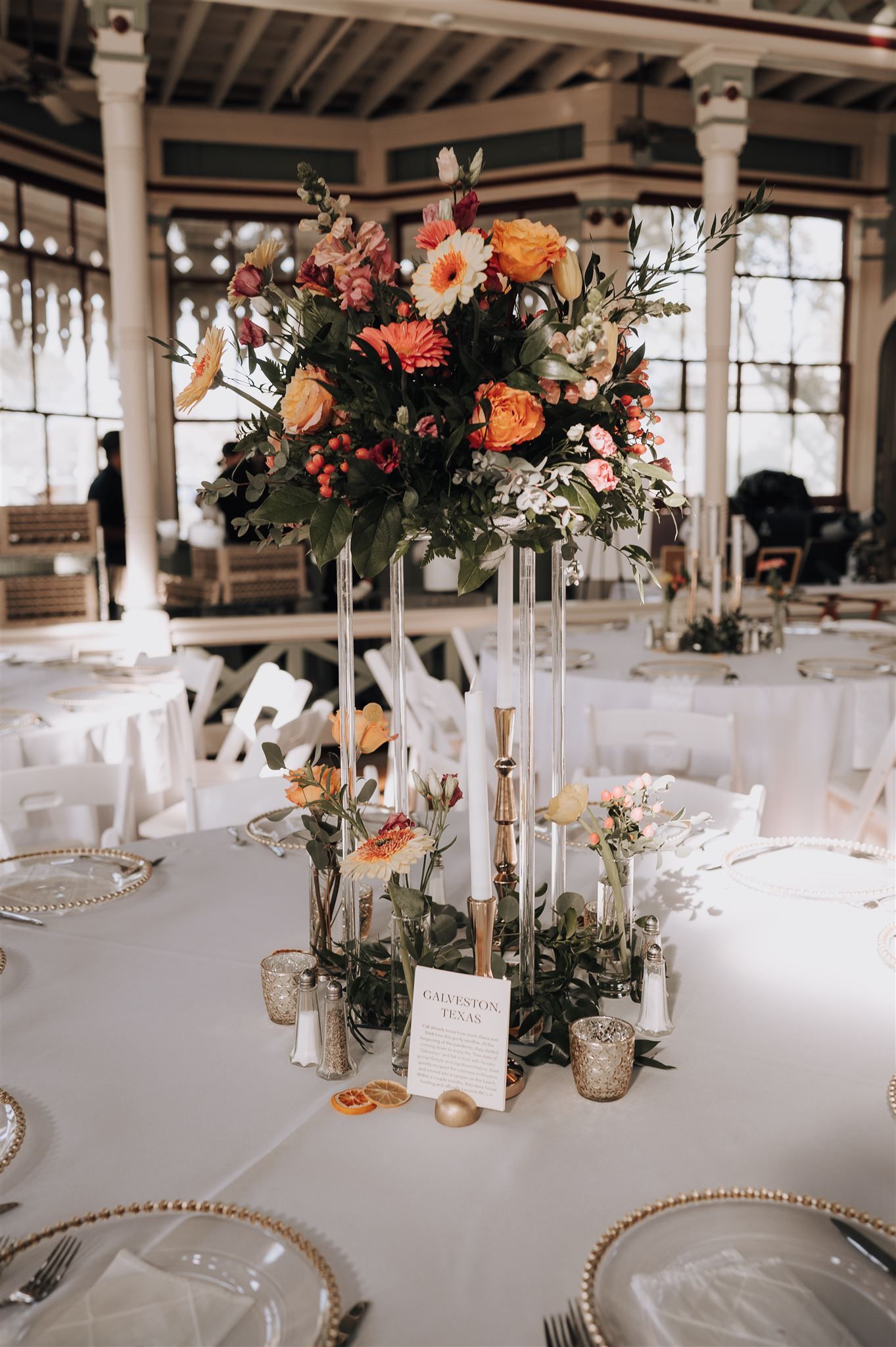 Elegant wedding table centerpiece with tall floral arrangement and white candles.