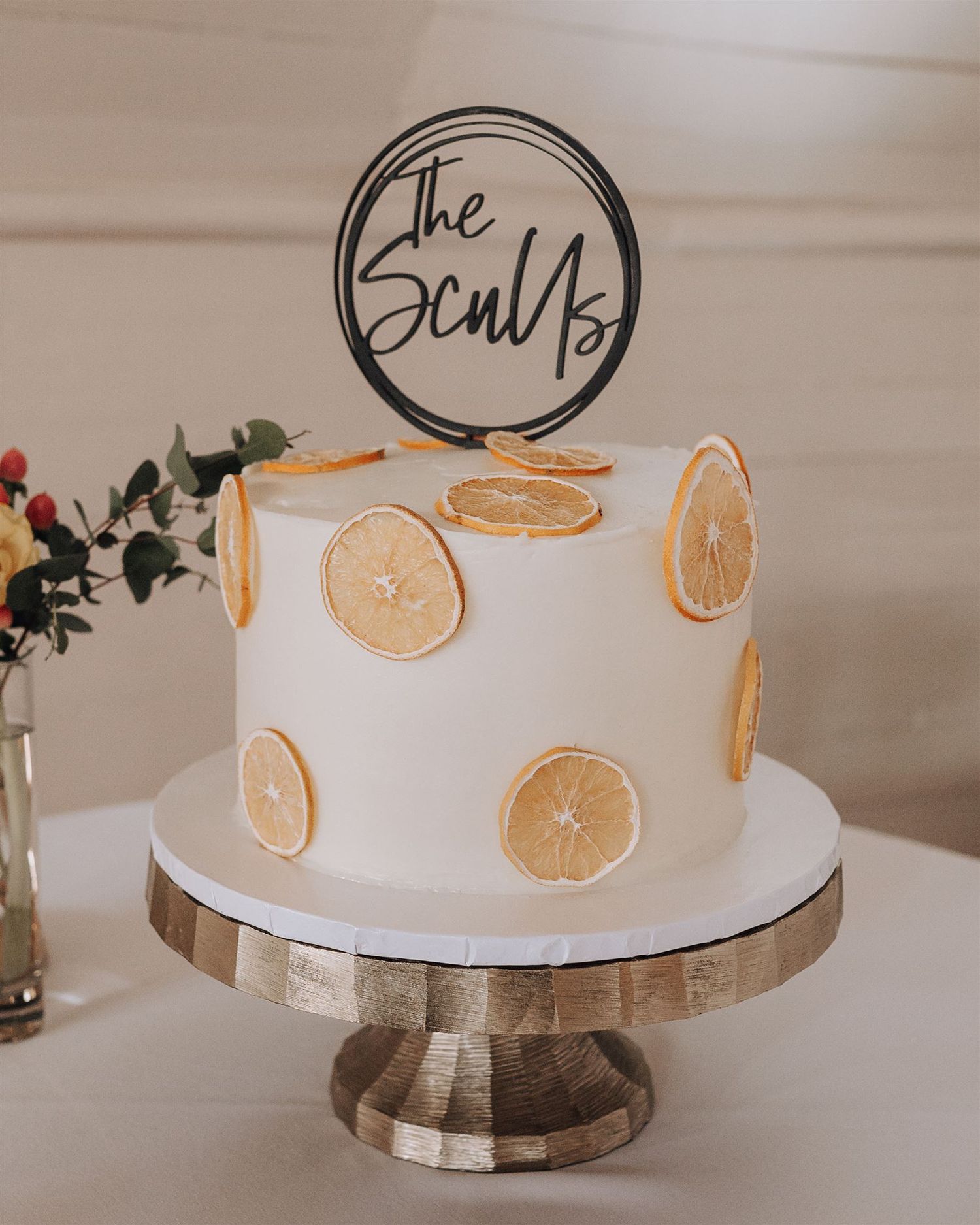 Modern white wedding cake with dried orange slices and The ScuVa logo topper.