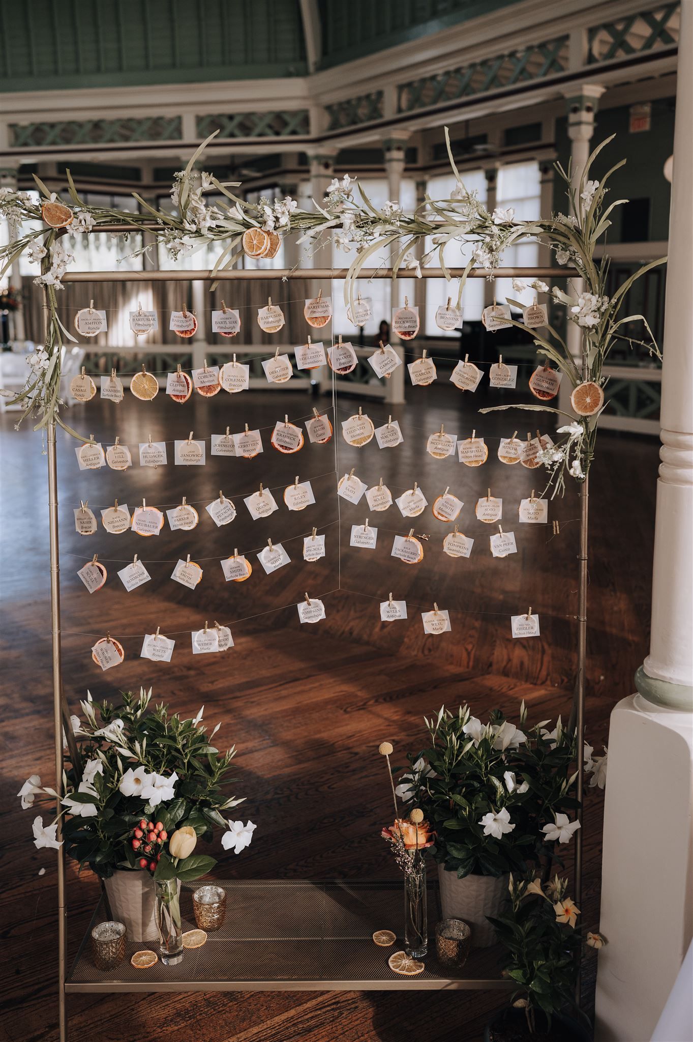 Wedding seating arrangement display with cards suspended on strings between decorative branches.
