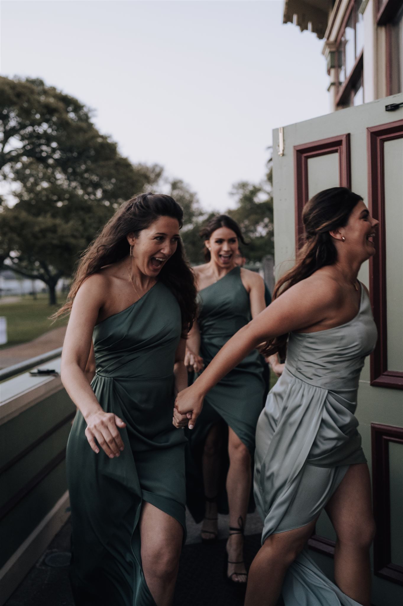 Bridesmaids in matching dresses laugh together on vintage train platform.