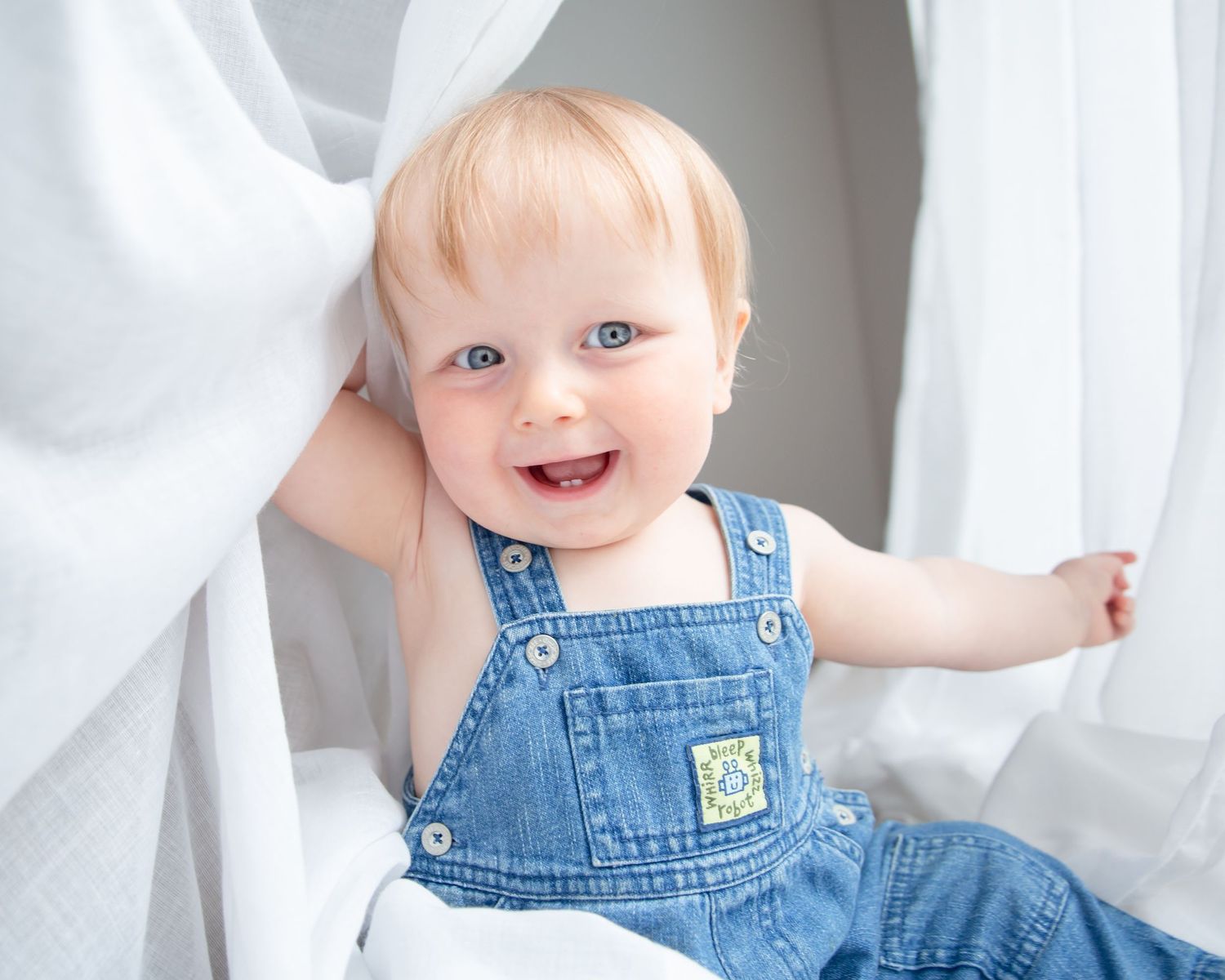 close up of smiling baby in dungarees with blue eyes