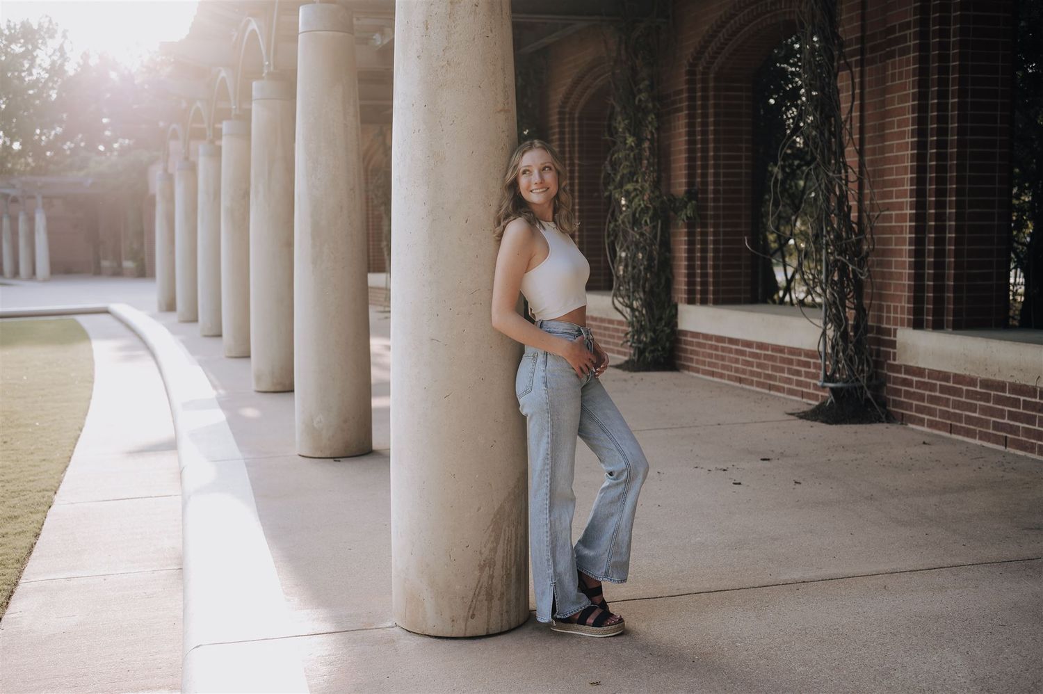 Elegant pose against columned architecture wearing light colored casual attire.